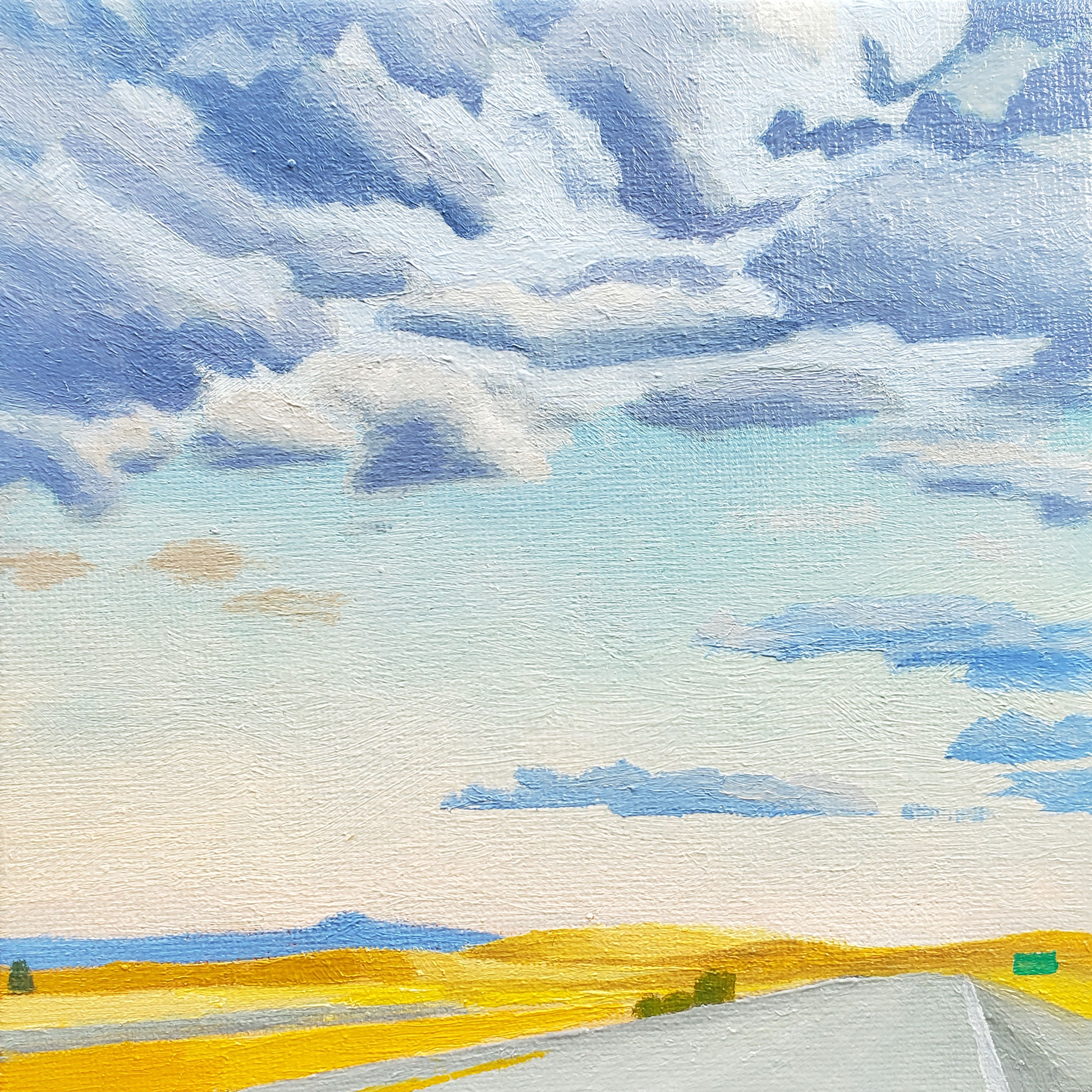 a sky mostly cleared of clouds above a freeway road and straw colored fields